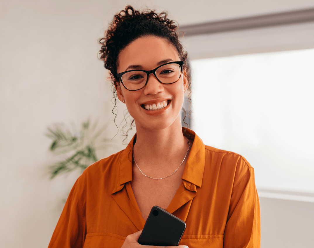 Mulher sorridente usando óculos e segurando um celular.