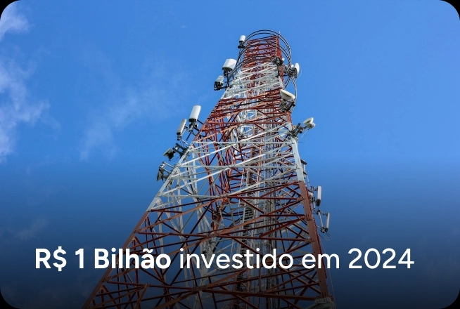 Uma torre de telecomunicações metálica vista de baixo para cima contra um céu azul limpo. Na base da imagem, o texto informa: "R$ 1 Bilhão investido em 2024".