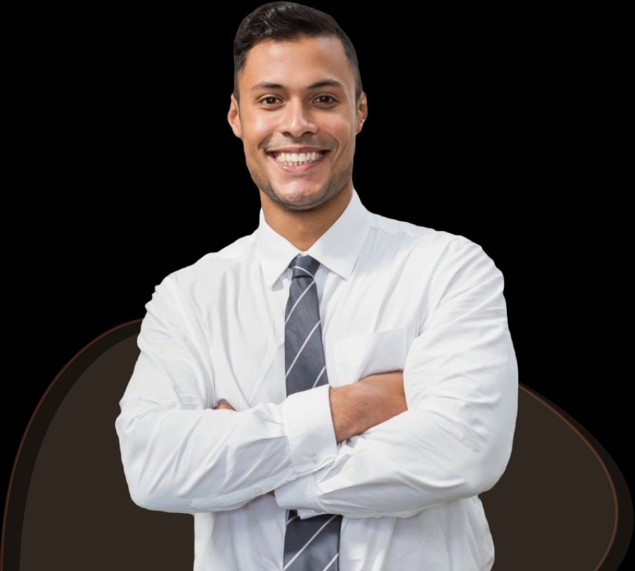 Um homem jovem com cabelo preto curto está sorrindo amplamente, vestindo uma camisa social branca e uma gravata cinza com listras diagonais. Ele está com os braços cruzados, transmitindo uma atitude amigável e confiante. Ele parece ser um profissional ou gerente.